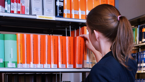 Eine Frau steht an einem Regal mit Büchern und kippt eines an, um es herauszunehmen.