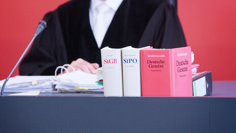 Ein Richter sitzt an einem Pult, auf dem verschiedene Gesetzesbücher stehen.