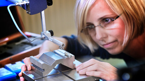 Eine Frau arbeitet an einem silbernen Werkstoff, der in eine Maschine eingespannt ist.